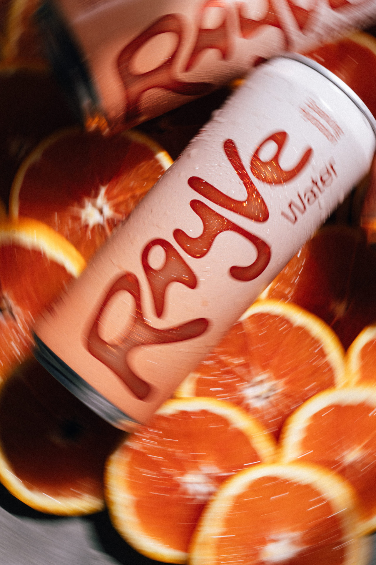 A Rayve Water can surrounded by sliced blood oranges with a vibrant motion-blur effect